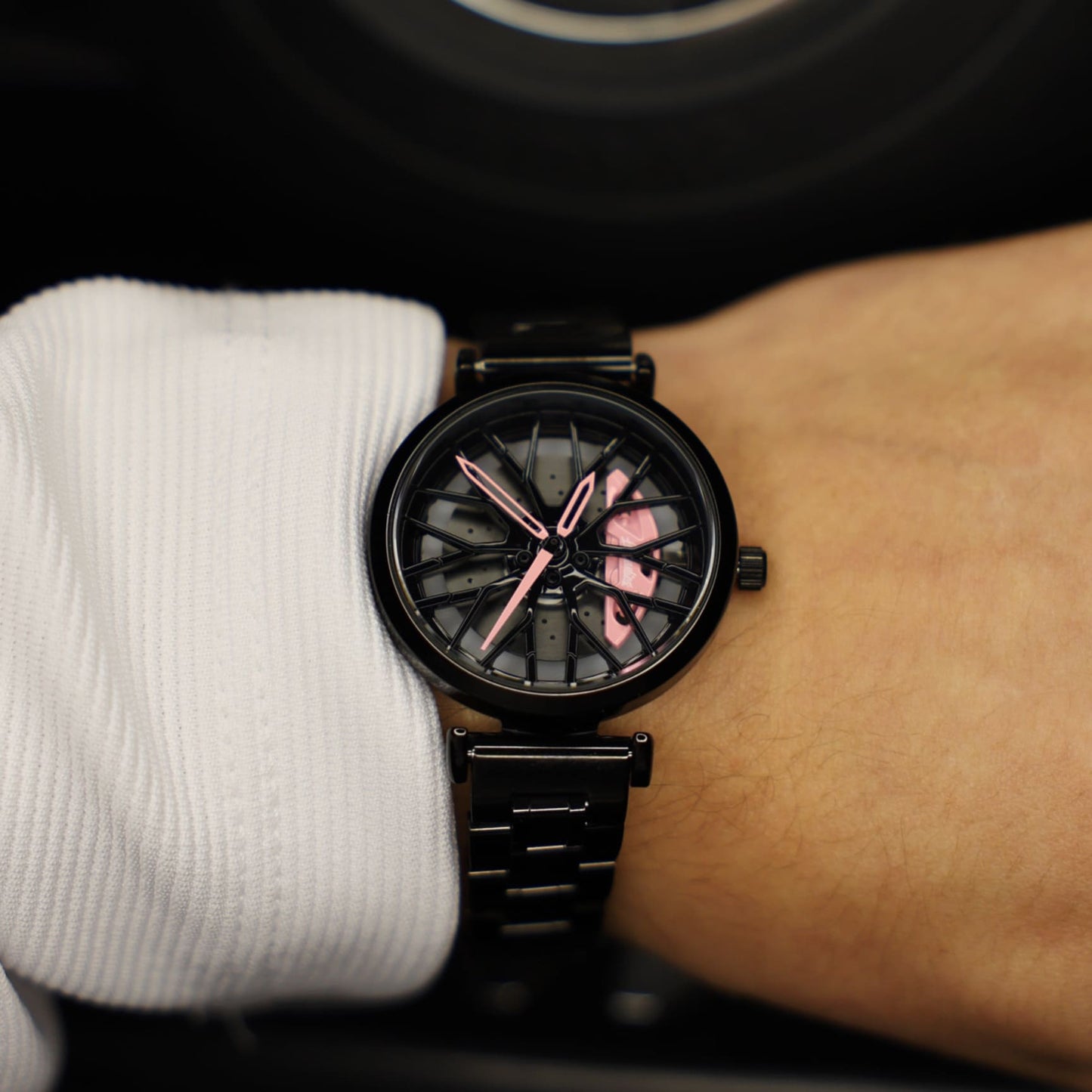 An image showcasing a DriftElement Lady Like Edition watch, a unique timepiece with a motorsport-inspired rim design. This innovative accessory from a young German startup features striking pink accents that contrast with the dark rim pattern, embodying a blend of sportiness and femininity.