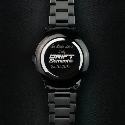 A custom-engraved black watch from DriftElement featuring the inscription 'In Liebe deine Lilly' above the brand's logo, with the date '23.10.2012' below. The image conveys a personalized touch on the back casing of the watch, signifying a special moment or dedication, characteristic of DriftElement's innovative wheel-inspired watch designs from Germany.