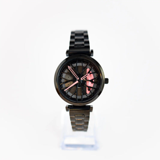 This image features the DriftElement Lady Like Edition, a women's wristwatch that elegantly combines motorsport aesthetics with feminine touches. The watch boasts a sleek, black metal band and body. The face of the watch is inspired by a car's rim, with a detailed, wheel-like design and eye-catching pink highlights on the hands and hour markers, adding a pop of color and style. This innovative design is emblematic of DriftElement, a young German startup that specializes in rim-design watches.