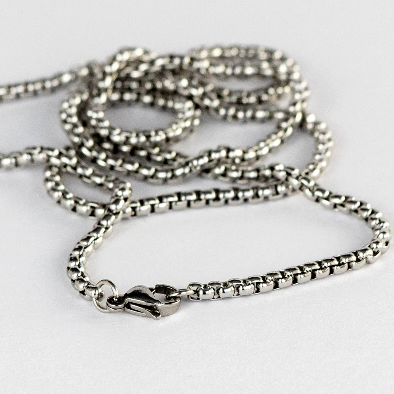 A close-up image displaying a fine silver chain with a detailed box link design, which catches light to create a subtle shimmer. The secure lobster claw clasp is also visible, indicating the functional and aesthetic care taken in the design of the jewelry. This piece reflects the elegant, minimalist style akin to DriftElement's innovative approach to watch design, incorporating automotive elements, as demonstrated by their unique wheel-inspired watches, from a creative startup based in Germany. 