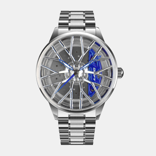 The image showcases a silver and blue motorsport-inspired watch by DriftElement, a youthful German startup. The watch features a striking rim-design dial with intricate wheel spoke detailing and vibrant blue accents. This innovative timepiece has a metallic silver bracelet and a sleek, contemporary look, reflecting the company's fusion of automotive enthusiasm and cutting-edge watch design.