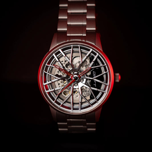A striking Motorsport EMS Edition automatic wristwatch by DriftElement, featuring a rim-inspired face with a complex mechanical movement visible through the spoke-like design. The watch has a sleek red and metallic silver color scheme, complete with a matching red-tinted crown and a sturdy metal bracelet, showcasing an innovative blend of automotive inspiration and advanced watchmaking.