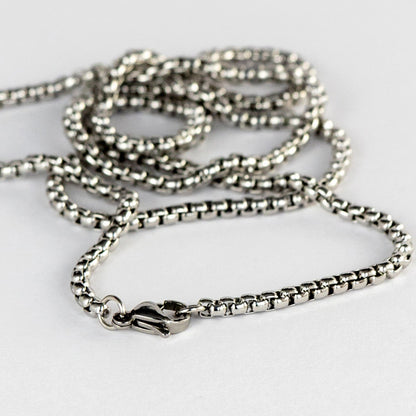 A close-up image displaying a fine silver chain with a detailed box link design, which catches light to create a subtle shimmer. The secure lobster claw clasp is also visible, indicating the functional and aesthetic care taken in the design of the jewelry. This piece reflects the elegant, minimalist style akin to DriftElement's innovative approach to watch design, incorporating automotive elements, as demonstrated by their unique wheel-inspired watches, from a creative startup based in Germany.