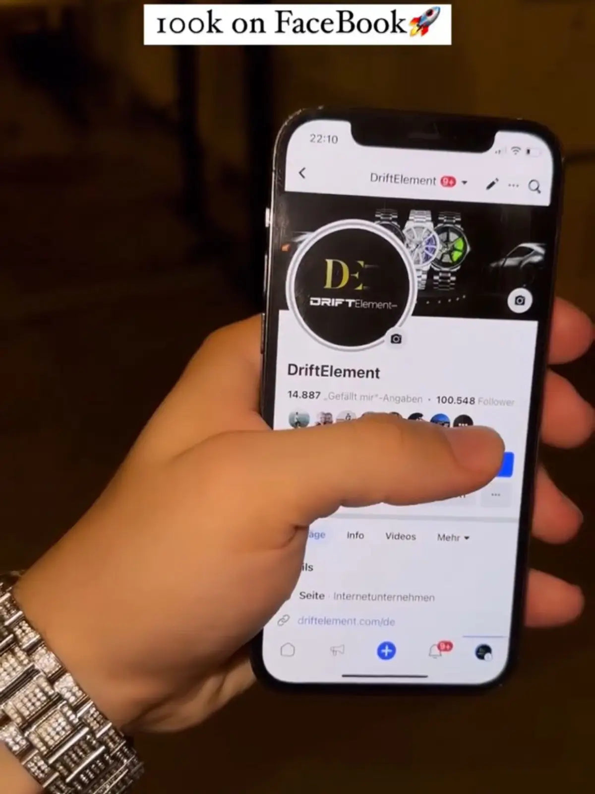 The image shows a person's hand holding a smartphone that displays DriftElement's Facebook page. On the screen, there's a profile picture of the DriftElement logo and a cover photo showcasing a selection of the brand's unique rim-designed watches, reflecting the company's innovative approach to watch design. The wrist of the hand holding the phone is adorned with a DriftElement watch featuring the signature rim design, suggesting a proud display of brand affiliation. 