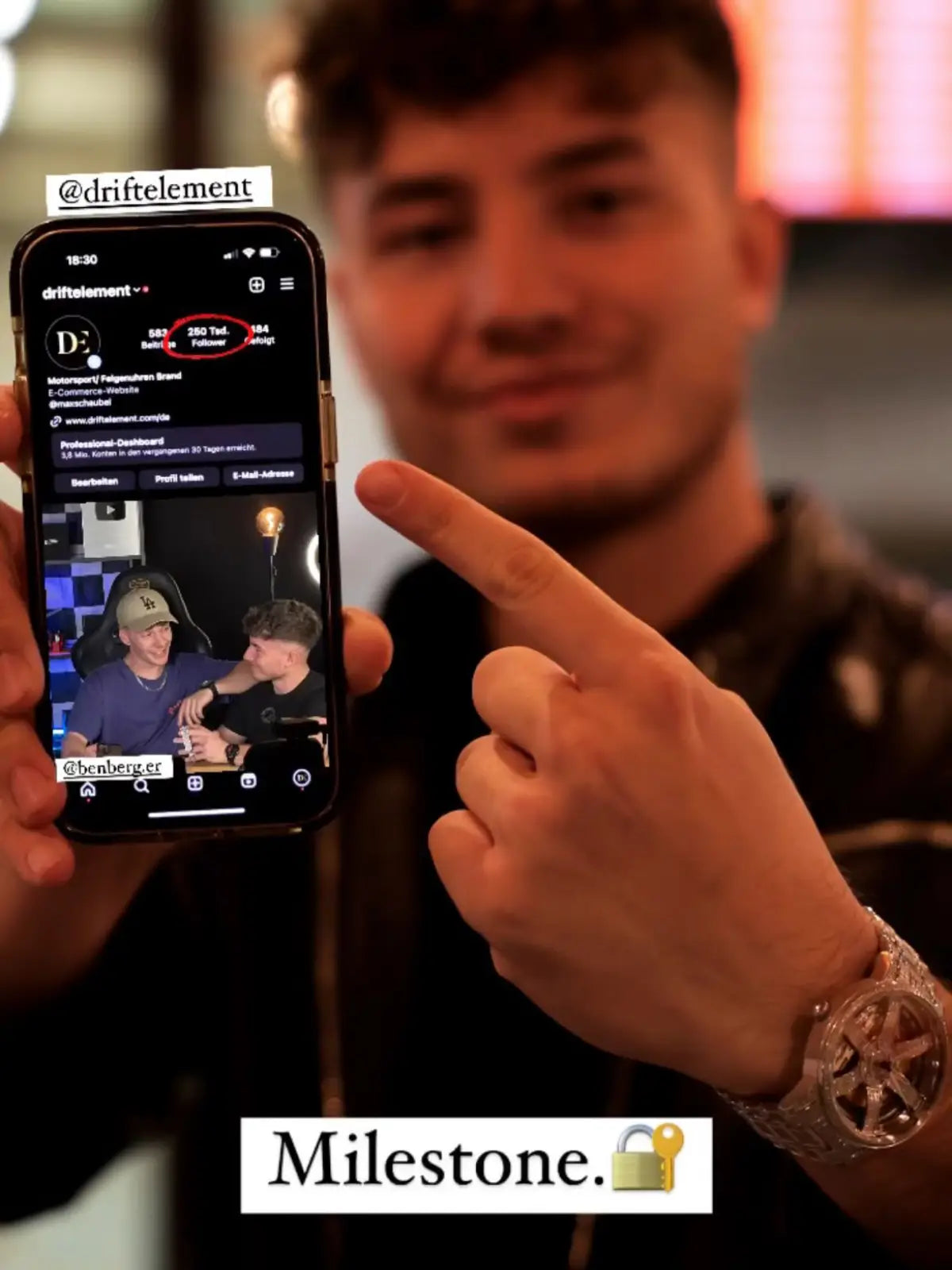 The image shows a young man proudly displaying a smartphone screen with the Instagram profile of @driftelement, a German startup that designs innovative wheel rim-themed watches. On his wrist is one of their watches, featuring the signature rim design, encrusted with what appears to be sparkling gemstones, exemplifying their unique blend of automotive inspiration and luxury. 
